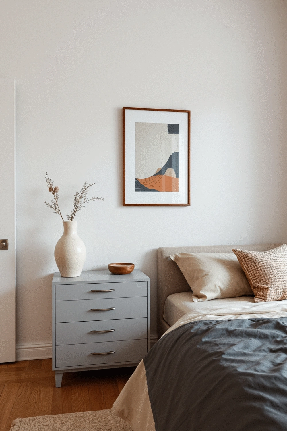 A minimalist bedroom with a framed abstract art piece on the wall, a unique ceramic vase on a simple dresser, and a decorative cushion on the bed, all in a cohesive color palette.